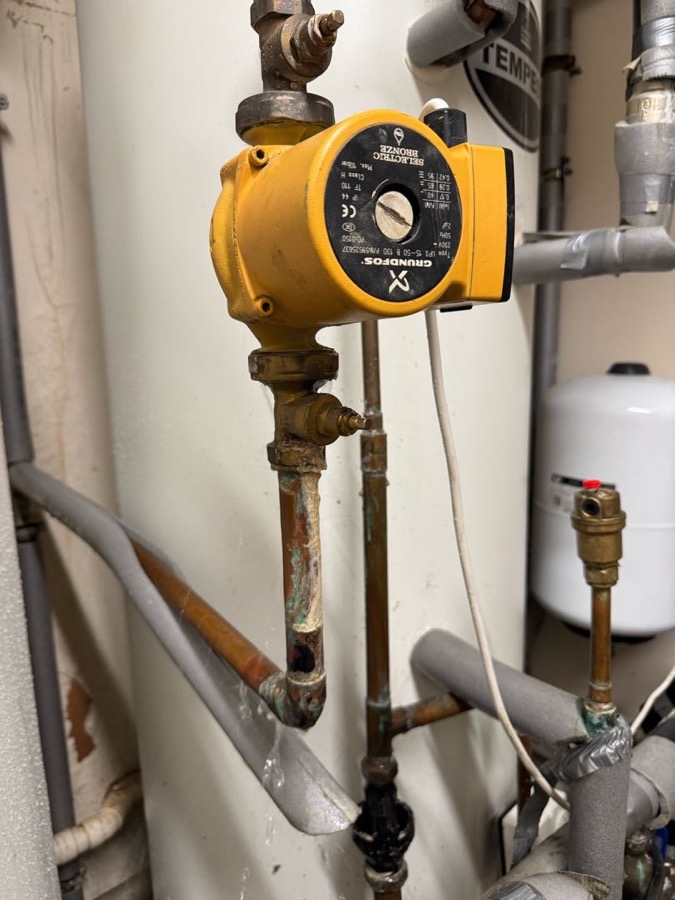 A circulating pump on copper pipework in a care home plant space, with green staining on the pipe below the union beneath it